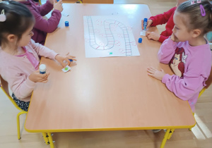 Dzieci siedzą przy stoliku i grają w samodzielnie przygotowaną grę z kasztanami