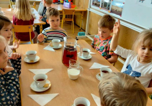 Dzieci siedzą przy stole i piją herbatę z filiżanek