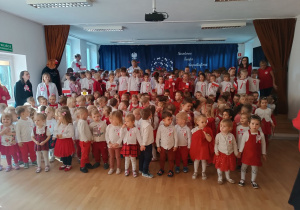 Dzieci ubrane na biało czerwowno śpiewają hymn