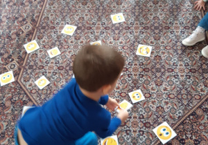 Na dywanie leżą karteczki z różnymi emotikonkami. Chłopiec podnosi jedną z nich.