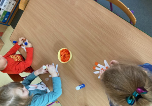 Dzieci przygotowują pomarańczowe rączki.